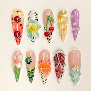 May include: Ten long, almond-shaped fake nails with different designs. The designs include ladybugs, flowers, cherries, seashells, and rhinestones.