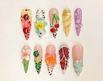 May include: Ten long, almond-shaped fake nails with different designs. The designs include ladybugs, flowers, cherries, seashells, and rhinestones.