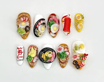 Könnte beinhalten: Zehn Miniatur-Nageldesigns mit Essensthema, darunter Ramen, Sushi und Eier. Die Designs sind auf weiße Nagelspitzen gemalt.