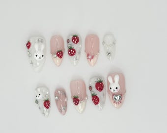 May include: Set of ten pink and white artificial nails with a strawberry and bunny rabbit theme. The nails are decorated with small rhinestones and 3D bunny rabbit and strawberry charms.