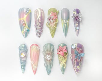 Puede incluir: Un conjunto de 12 puntas de uñas iridiscentes con varios diseños florales y de mariposas en 3D. Las puntas son en tonos de rosa, azul, verde y morado.