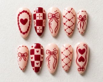 May include: A set of ten artificial nails in various designs. The nails are primarily a light pink color with dark red accents. Designs include hearts, bows, and checkered patterns. The nails are arranged on a white surface.