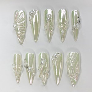 May include: Ten white, long, pointed fake nails with different pearl and rhinestone embellishments.