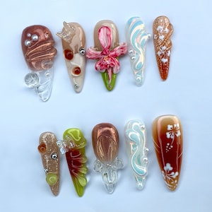 May include: Ten different nail art designs on a white background. The designs include flowers, swirls, and abstract patterns. The colours used are brown, pink, white, and green.