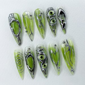 May include: Set of ten green and silver nail tips with various designs, including swirls, eyes, and branches.