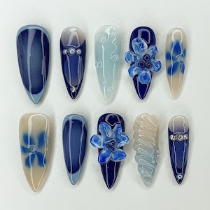 May include: Ten blue and white nail tips with different designs. Some have a swirl pattern, some have a flower design, and some have a simple blue and white ombre design.