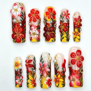 May include: A set of ten artificial nails, each adorned with 3D floral designs. The nails feature a base of yellow and white, with red, white, and yellow flowers, green leaves, and gold accents. The nails are arranged on a white surface.