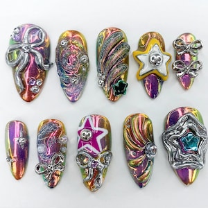 May include: Ten iridescent nail tips with various 3D embellishments, including stars, bows, and swirls. The nail tips are decorated with silver, gold, and white accents.