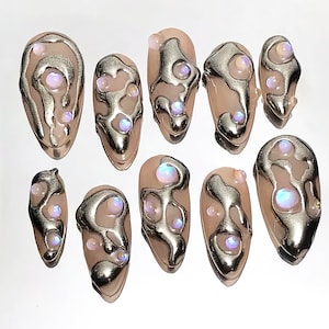 May include: Set of ten false nails with a pink base and silver metallic swirls. Each nail is adorned with iridescent opal-like gems.