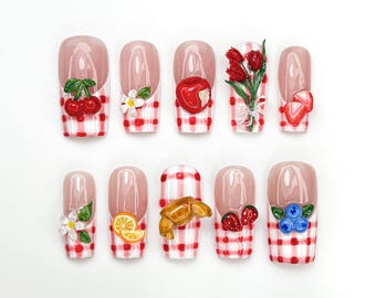 May include: A set of ten artificial nails with a clear base and red and white gingham pattern. Each nail features a different 3D design, including cherries, flowers, an apple, tulips, strawberries, an orange slice, a croissant, and blueberries.