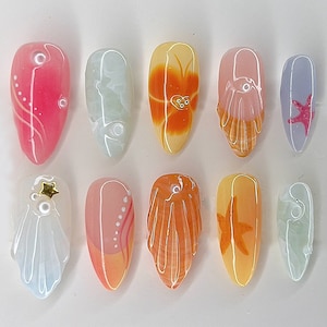 Könnte beinhalten: Eine Sammlung von zehn künstlichen Nägeln, jeweils mit einem einzigartigen Design. Die Nägel weisen verschiedene Farben auf, darunter Rosa, Orange und Blau, mit dekorativen Elementen wie einem Seestern, einer Blume und abstrakten Mustern. Die Nägel sind oval geformt.