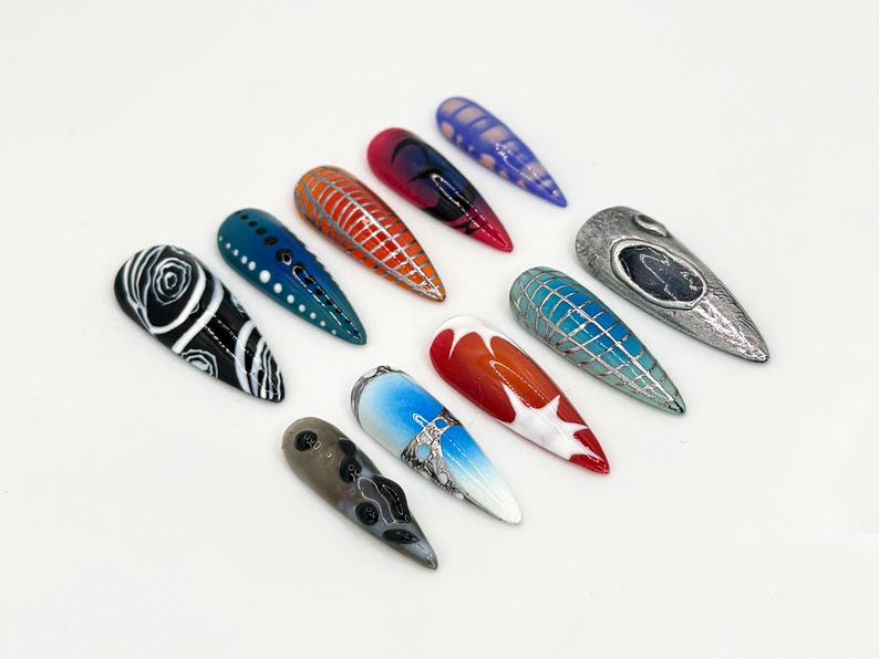May include: Ten long, almond-shaped false nails with various designs. The designs include black and white swirls, blue and white dots, red and white stripes, a silver and blue geometric pattern, a red and white ombre, a blue and white ombre, a silver and blue geometric pattern, a silver and black design, a silver and blue geometric pattern, and a silver and black design.