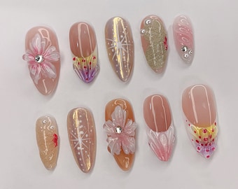 May include: Ten nude-coloured artificial nails with various designs. Some nails feature delicate floral accents, while others have intricate patterns and glitter accents.
