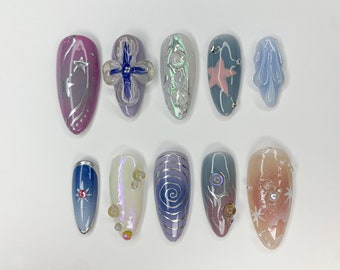 Puede incluir: Diez diseños de uñas diferentes que presentan una variedad de colores, patrones y adornos. Los diseños incluyen una uña rosa con estrellas plateadas, una uña azul con una estrella plateada, una uña blanca con espirales plateadas y una uña rosa con una estrella plateada.
