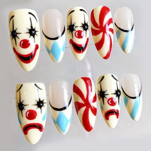 Peut inclure: Ensemble de dix faux ongles avec diff&eacute;rents motifs. Cinq ongles pr&eacute;sentent un visage de clown avec des l&egrave;vres rouges, des yeux noirs et un nez rouge. Trois ongles pr&eacute;sentent un motif en spirale bleu et blanc. Deux ongles pr&eacute;sentent un motif de canne en sucre rouge et blanc.