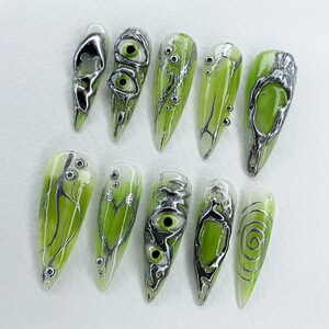 May include: Ten green and silver nail art designs. The designs feature swirls, eyes, and branches.