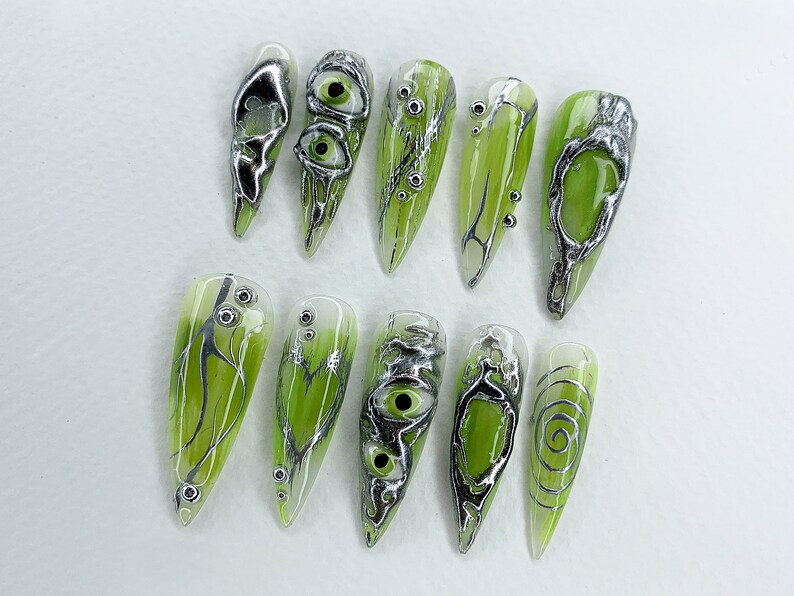 May include: Ten green and silver nail art designs. The designs feature swirls, eyes, and branches.