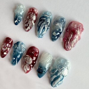 May include: Set of ten false nails with a gradient design in shades of blue, red, and white. Each nail features a silver glitter design and a 3D embellishment.
