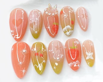 May include: Ten peach-colored almond-shaped fake nails with white and red designs. Some nails have a strawberry design, others have a flower design, and others have a swirl design. The nails are decorated with small white pearls.