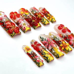May include: A set of press-on nails with a floral design. The nails feature a variety of colors, including red, yellow, and white, with intricate flower details and embellishments. The nails are arranged on a white surface.