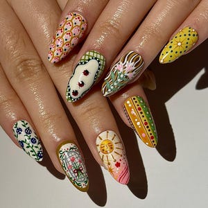 May include: A set of long, almond-shaped nails, each painted with unique designs. The designs include ladybugs, floral patterns, suns, and geometric shapes in a variety of colors, including pink, yellow, green, and white. The nails are well-manicured and showcase intricate nail art.