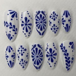 Puede incluir: Diez uñas postizas blancas y azules con un diseño tradicional de azulejos Talavera mexicanos. Las uñas son largas y puntiagudas.