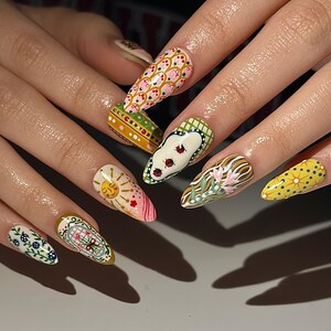 May include: A set of long, almond-shaped fingernails, each painted with a unique design. The designs include floral patterns, suns, and geometric shapes in a variety of colors, including pink, yellow, green, and white. The nails are well-manicured and showcase intricate nail art.