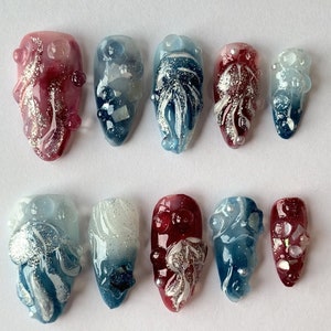 May include: Set of ten false nails with a gradient design. The nails are decorated with white and silver swirls, and some have small pearl-like embellishments. The nails are in two color schemes: blue and white, and red and white.