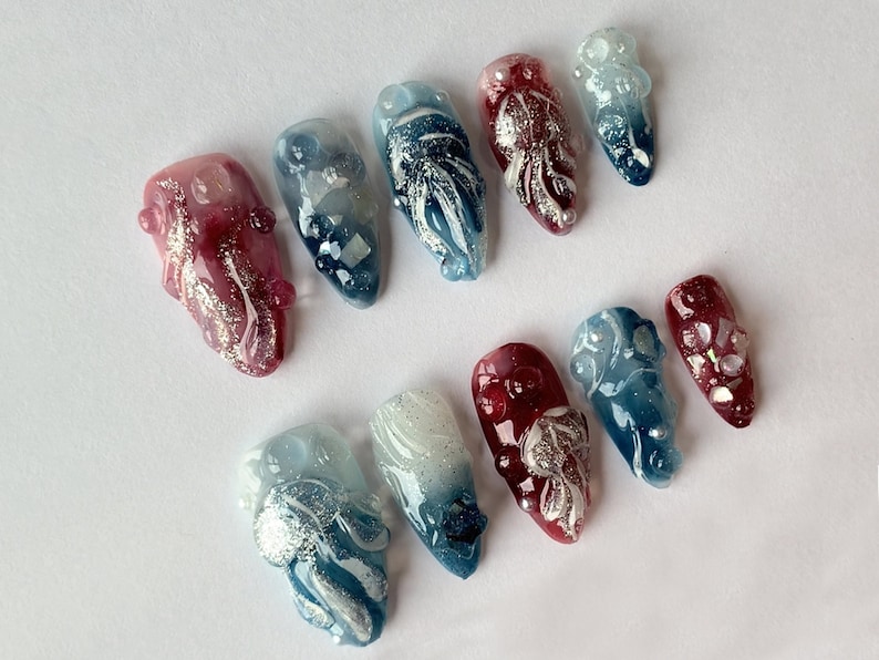 May include: Set of ten false nails with a marbled design. The nails are in shades of red, blue, and white with silver glitter accents.