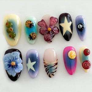 May include: Ten different nail designs featuring various themes, including ladybugs, olives, flowers, a star, a pool ball, a lemon, and tomatoes.