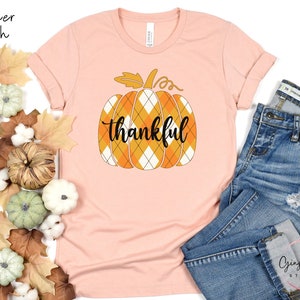 May include: A heather peach t-shirt with a graphic of a plaid pumpkin with the word "thankful" on it.