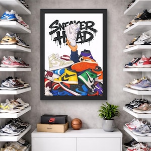 Może przedstawiać: Oprawiony wydruk z napisem "SNEAKER HEAD" w czarnym, ociekającym krojem pisma, z dłonią trzymającą białą tenisówkę. Wydruk otoczony jest kolekcją kolorowych tenisówek. Półki po obu stronach prezentują różne tenisówki, z piłką do koszykówki i rośliną na białej szafce.
