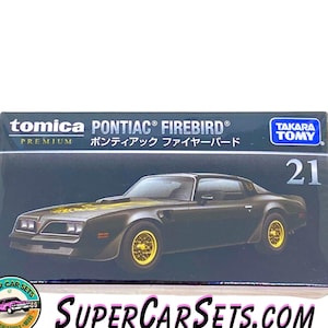 May include: A black Tomica Premium die-cast model car of a Pontiac Firebird with gold wheels. The box has the text "PONTIAC® FIREBIRD®" and "ポンティアック ファイヤーバード" in Japanese. The box also has the Tomica and Takara Tomy logos.