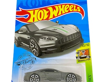 May include: A grey Hot Wheels Aston Martin DBS die-cast toy car in a blue and green blister pack. The car is part of the Hot Wheels HW Exotics series and is numbered 224/250. The packaging includes the Hot Wheels logo and the text "It's not the same without the same".