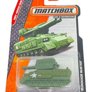 Könnte beinhalten: Grüner Spielzeug-Panzer mit einem großen Geschütz auf dem Dach. Der Panzer hat einen weißen Stern an der Seite und die Worte "Blockade Buster" auf der Verpackung. Matchbox On A Mission.