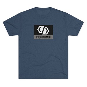 Può includere: Una t-shirt blu scuro con una grafica in bianco e nero di parentesi graffe di codice e la parola "PROGRAMMATORE" in testo bianco su sfondo grigio.