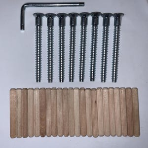 May include: A set of furniture assembly hardware, including eight silver screws, a metal Allen wrench, and a row of wooden dowels. The screws have a flat head and a threaded shaft. The dowels are light brown.