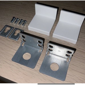 May include: Two sets of metal brackets with screw holes, each set includes two white plastic brackets and four screws. The brackets are designed for mounting curtains or blinds.