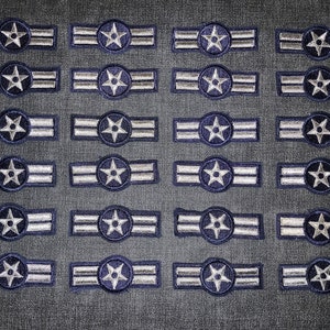 Puede incluir: Veinticuatro parches bordados en plata y azul con una estrella de cinco puntas en el centro y dos rayas plateadas.