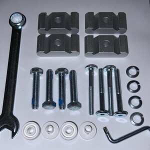 May include: A collection of metal hardware components, including a wrench, bolts, washers, and brackets. The items are arranged on a white surface, showcasing their silver color and various shapes. The image highlights the tools and parts.