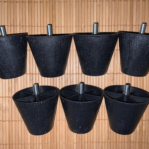 May include: Set of seven black, cone-shaped furniture legs with metal threaded studs for attachment. The legs are made of a textured, solid material and are arranged on a bamboo mat.
