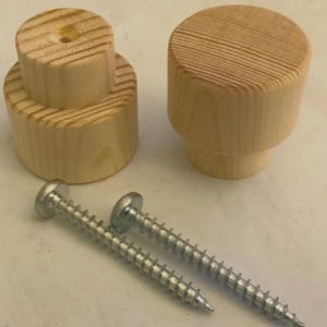May include: Two unfinished light-colored wooden knobs with a cylindrical shape and visible wood grain patterns, accompanied by two silver-colored metal screws with threaded shanks and rounded heads for installation purposes.