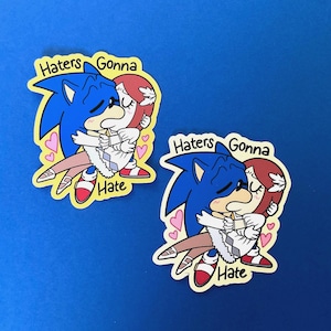 May include: Two stickers featuring a cartoon hedgehog and a woman embracing. The blue hedgehog has closed eyes and is kissing the woman with red hair. The text "Haters Gonna Hate" is above the characters.