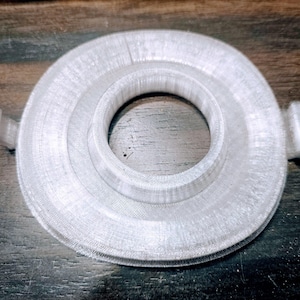 May include: White plastic ring with a raised center and two small tabs on the sides. The ring has a smooth, slightly textured surface.