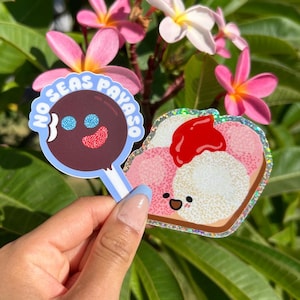 Peut inclure: Deux autocollants color&eacute;s, l'un avec une sucette brune aux yeux bleus et le texte "No Seas Payaso" et l'autre avec un toast de dessin anim&eacute; rose et blanc avec de la confiture rouge et un visage heureux.