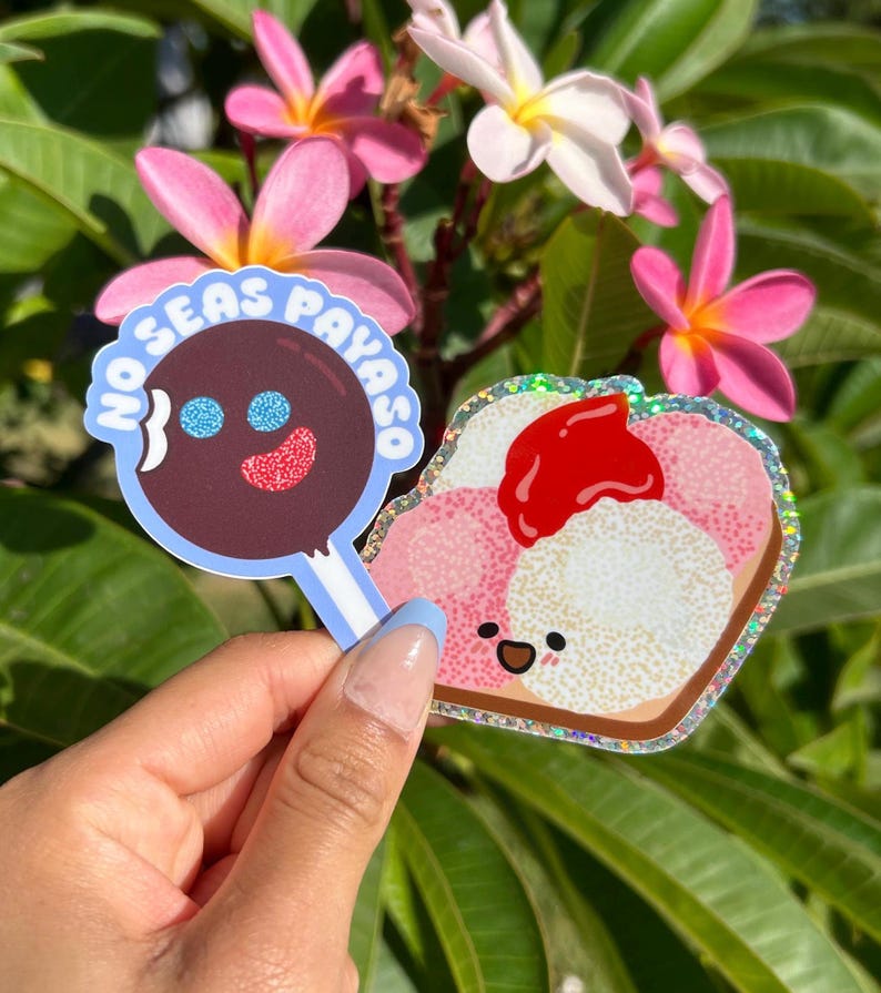 Peut inclure: Deux autocollants color&eacute;s, l'un avec une sucette brune aux yeux bleus et le texte "No Seas Payaso" et l'autre avec un toast de dessin anim&eacute; rose et blanc avec de la confiture rouge et un visage heureux.