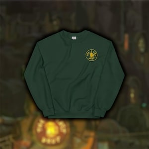 Pode incluir: Uma camisa de frio verde escura com um logotipo bordado amarelo que diz "The Last Drop" no peito esquerdo.