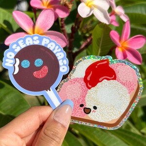 Peut inclure: Deux autocollants, l'un avec une sucette brune avec un visage bleu et rouge et le texte "No Seas Payaso" dans un cercle bleu, et l'autre avec un toast de dessin anim&eacute; rose et blanc avec une fraise rouge sur le dessus et un visage heureux.