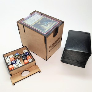 May include: A wooden card storage box with a card visible on top, a small dice box, and a stack of black card sleeves. The box has the words "MAGIC THE COMMANDER" printed on the side. The dice box contains various coloured dice.