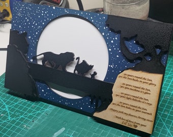 May include: A layered wooden frame featuring a silhouette of characters from a popular animated film. The background is a starry night sky with a large white circle. A poem is engraved on a wooden plaque.